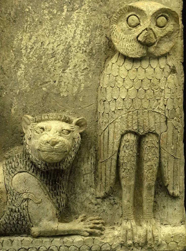 an animal statue sitting next to a cat on top of a stone slab in front of a wall