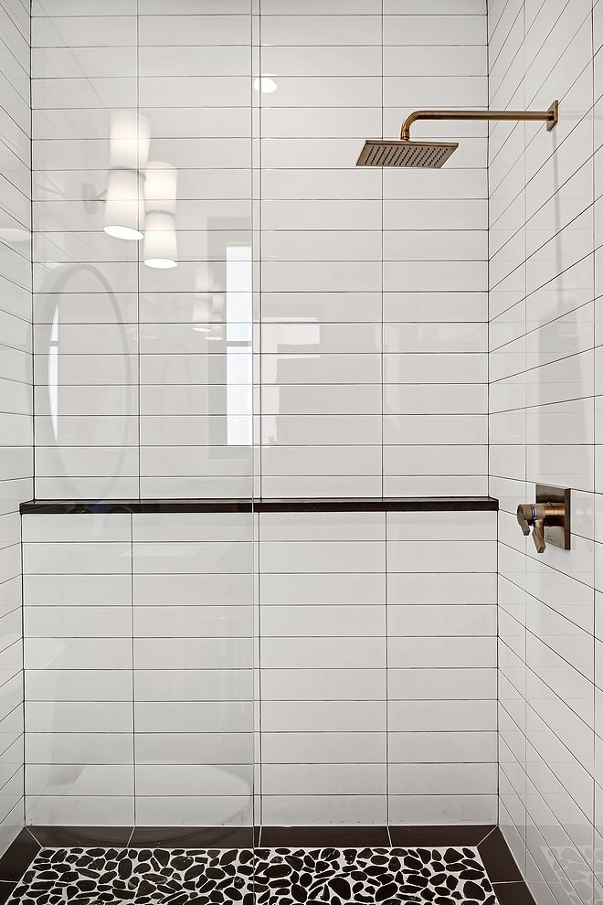 a white tiled bathroom with black and white flooring, shower head, and rug