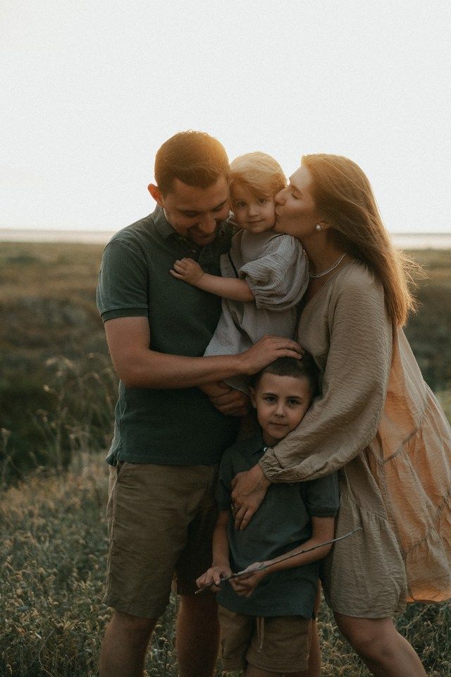 a man and woman with two children hugging each other in the middle of a field