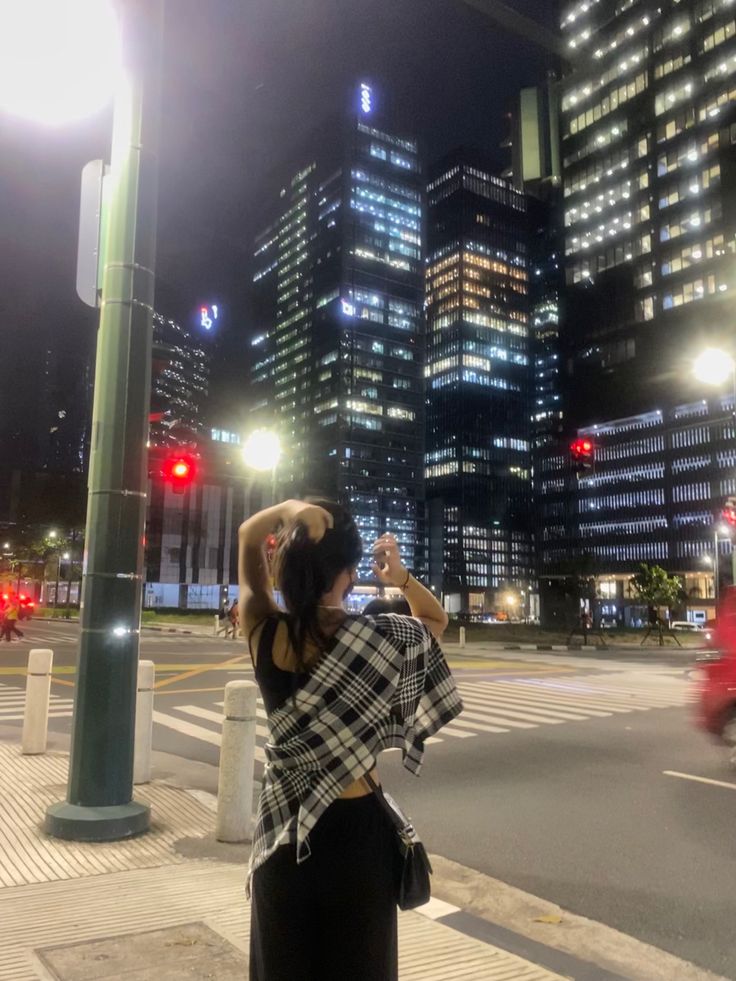 a woman standing on the side of a street at night taking a photo with her cell phone