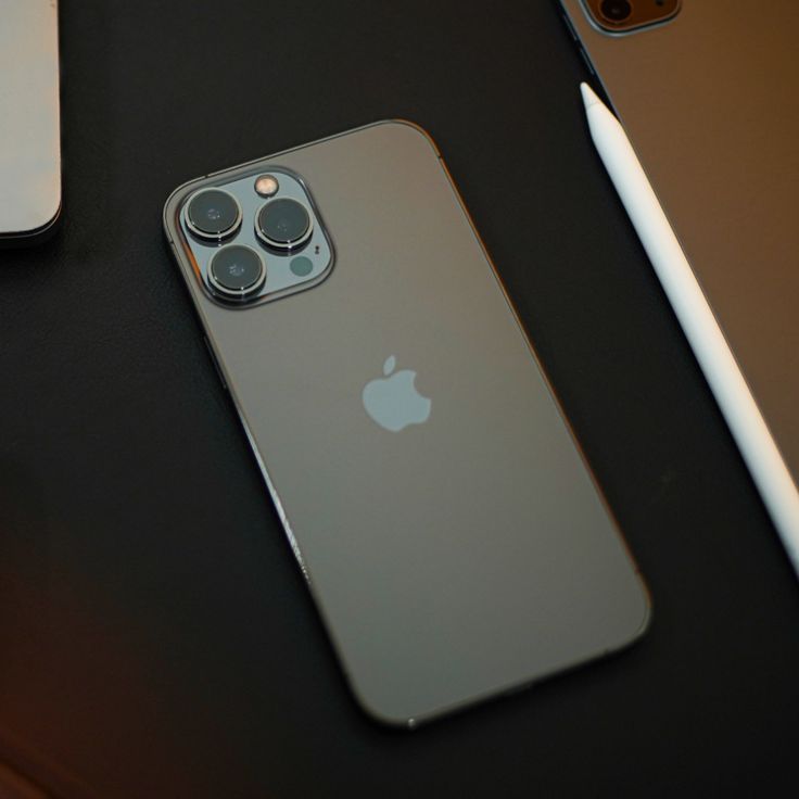 two iphones sitting next to each other on top of a black table with an apple pen