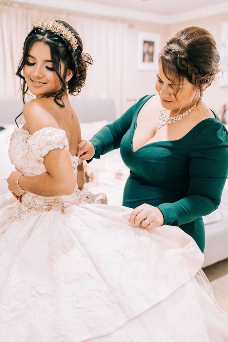 two women in dresses are helping each other put on their wedding dress