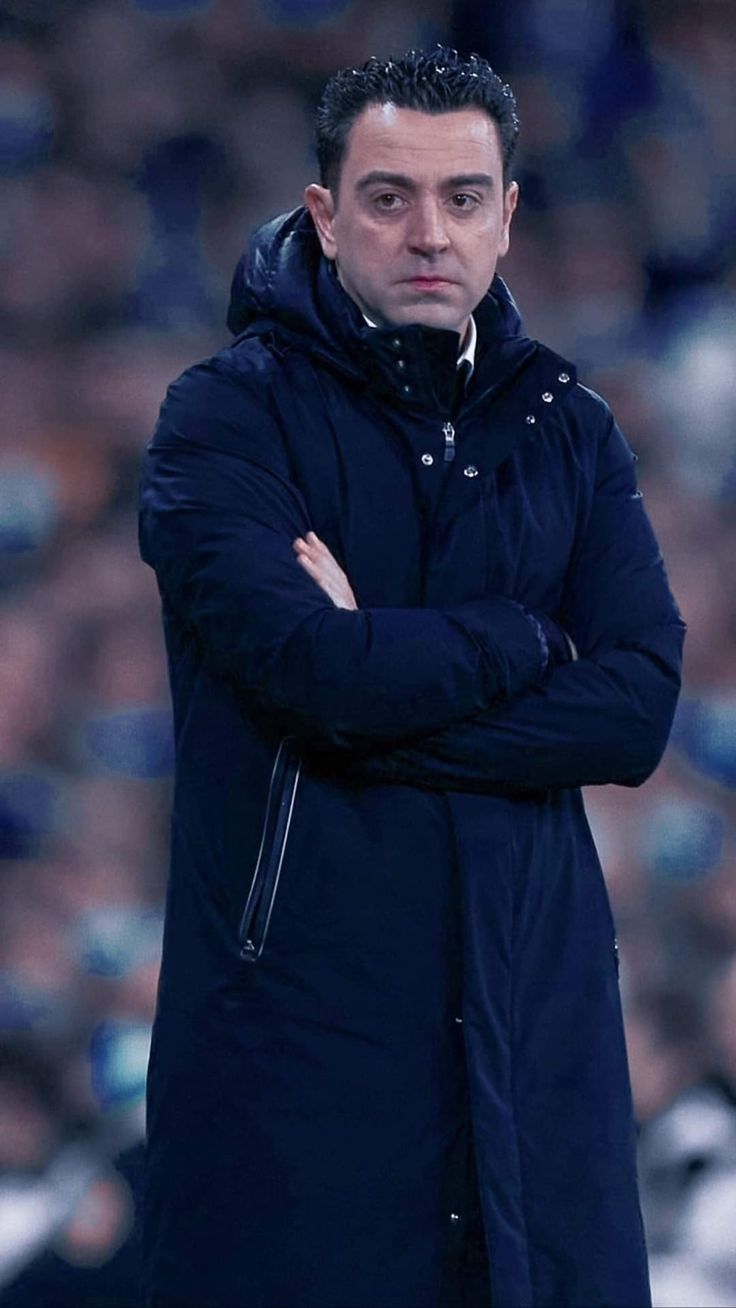 a man standing on top of a soccer field wearing a blue coat and holding his arms crossed