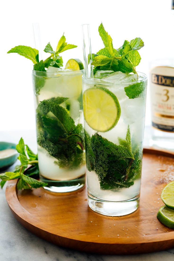 two glasses filled with mojitos sitting on top of a wooden table