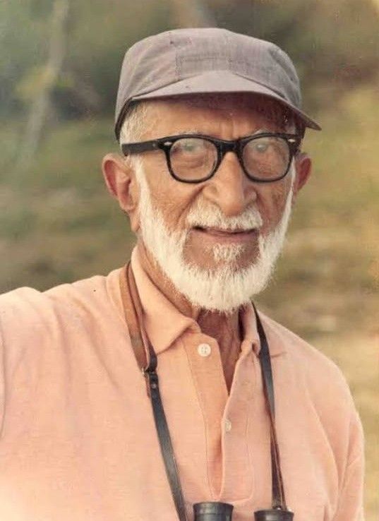 an old man with glasses and a hat holding two camera's in his hands