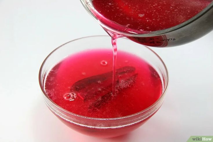 a pitcher pouring red liquid into a glass filled with water on top of a white table