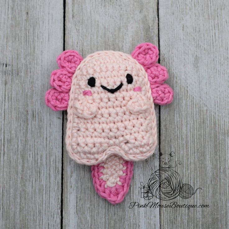 a crocheted pink and white stuffed animal laying on top of a wooden floor