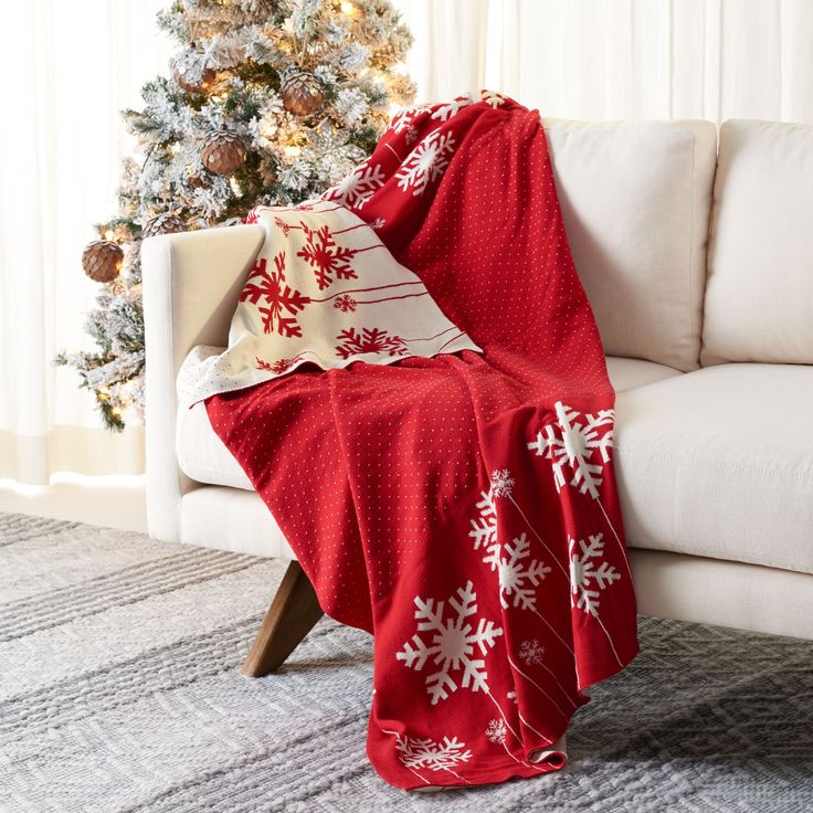 a white couch sitting next to a christmas tree covered in red and white snowflakes