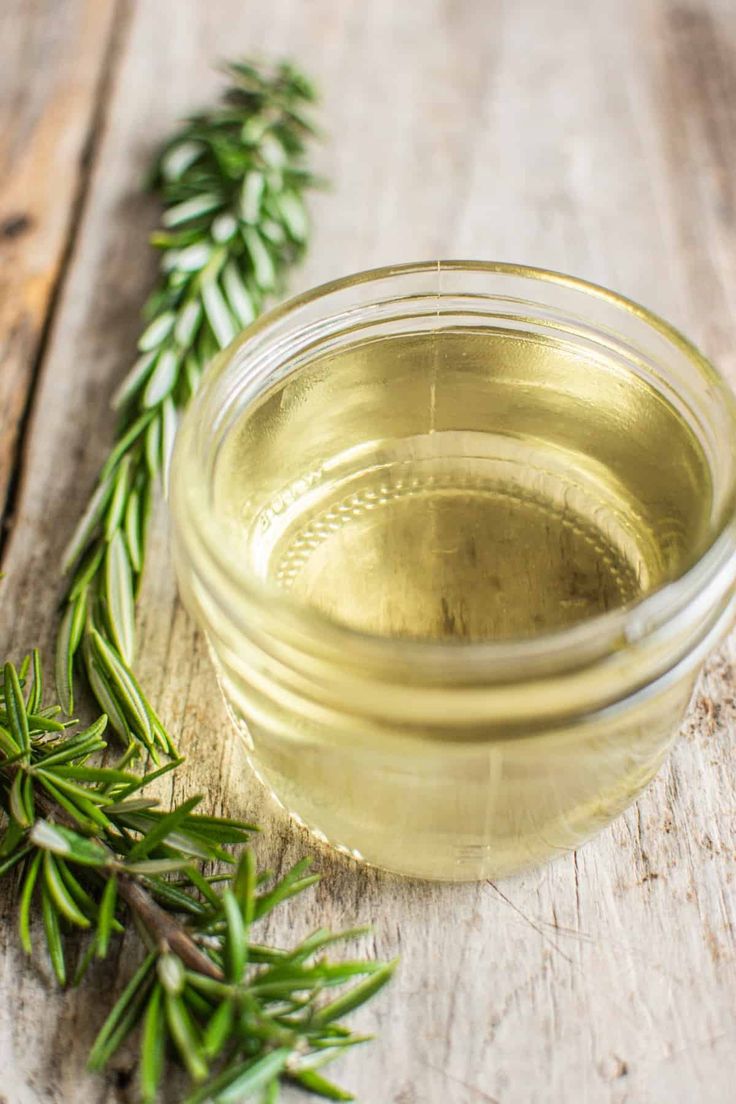 a glass jar filled with olive oil next to some rosemary sprigs on a wooden table