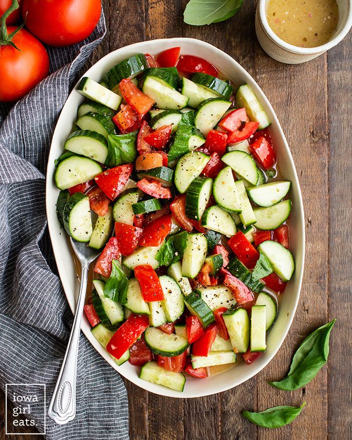 a bowl filled with cucumbers and tomatoes next to some sauce on the side