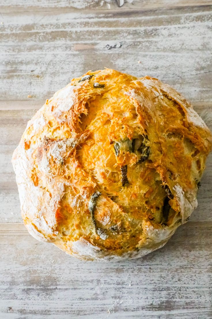 a loaf of bread sitting on top of a wooden table covered in cheese and spinach