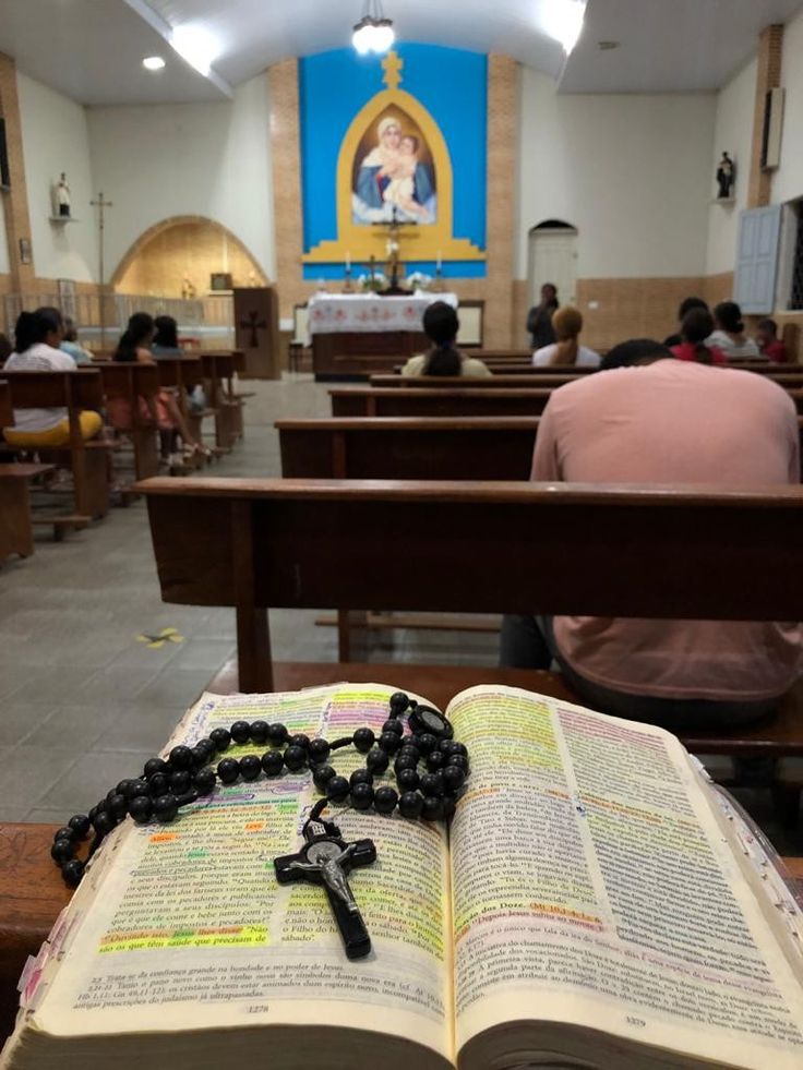 an open bible and rosary on a table in a church with people sitting at the pews