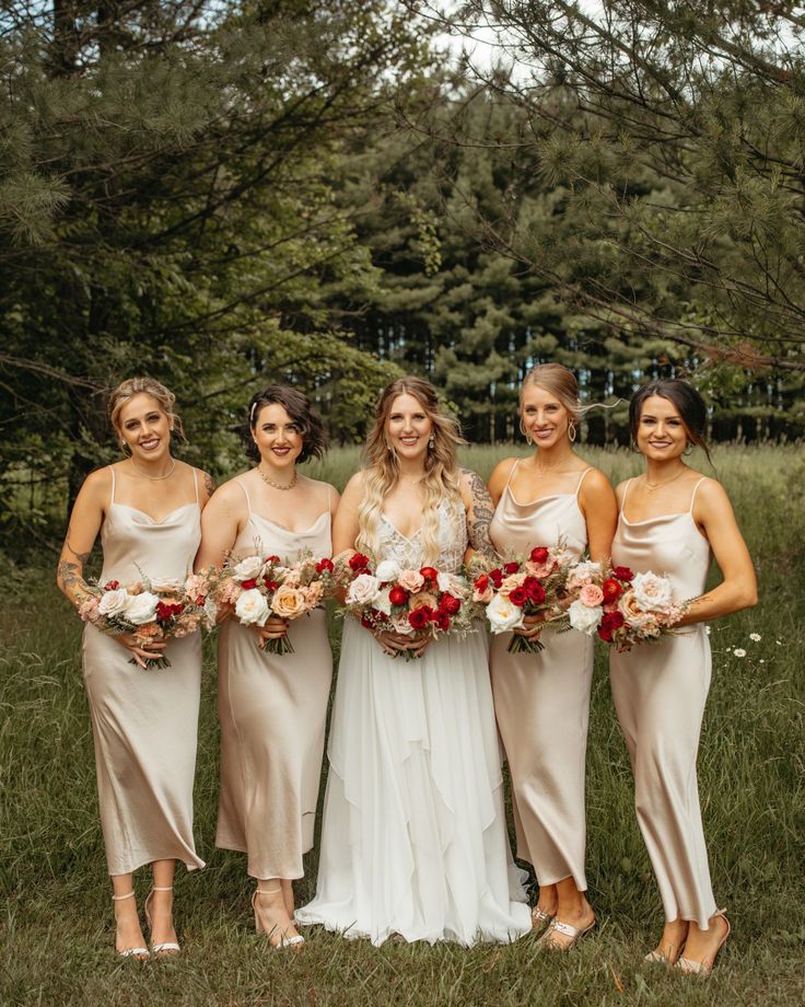 a group of women standing next to each other holding bouquets in front of trees