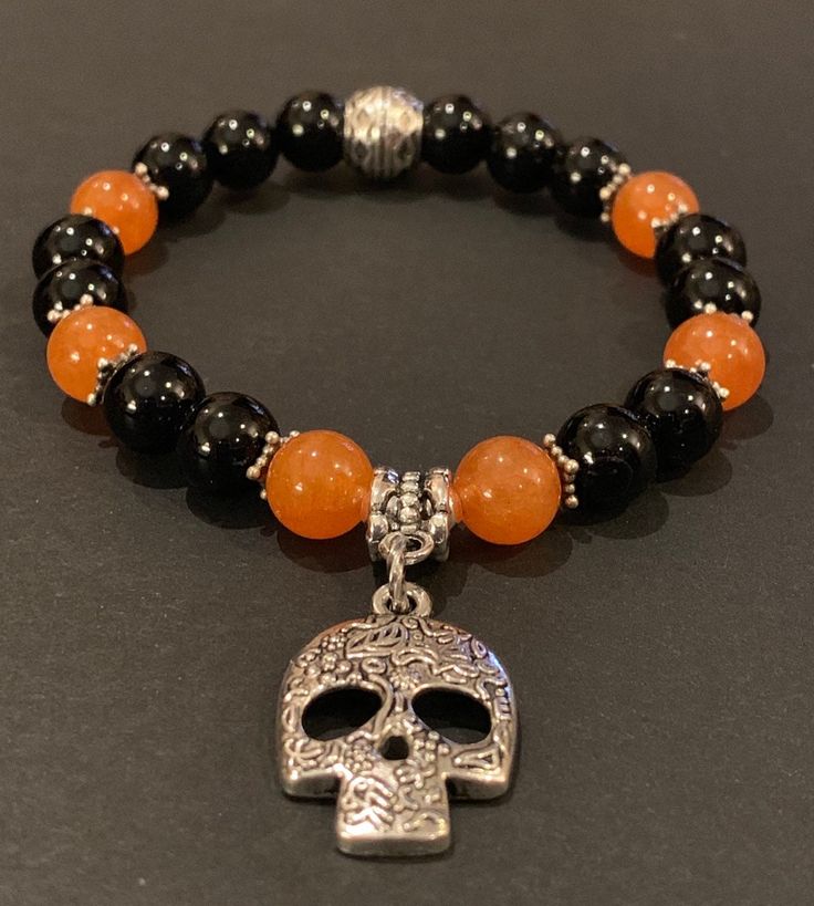 This fun to wear Halloween Theme charm bracelet features 8mm black onyx and orange quartz beads with antique silver spacers and barrel bead. The beautiful 25mm antique silver sugar skull charm really makes this a great bracelet to celebrate Halloween, Dia de los Muertos or anytime that makes you happy. An additional selection of charms is available in the pull down menu. The bracelet is strung on 1mm Ninja stretch cord and easily rolls over your hand to rest on the wrist. The 6.5 inch bracelet is featured in the photograph of my hand but I can custom make any size you need. Just select the size you need or convo me with your special request. Please know that each bracelet I make is truly one-of-a-kind and made with a Touch of Magick. To determine what size you need, use a tape measure, or Halloween Beaded Bracelet, Halloween Bracelet Ideas, Skull Bead Jewelry, Halloween Beaded Jewelry, Heishi Jewelry, Halloween Sugar Skull, Orange Quartz, Clay Bracelets, Bracelet Craft