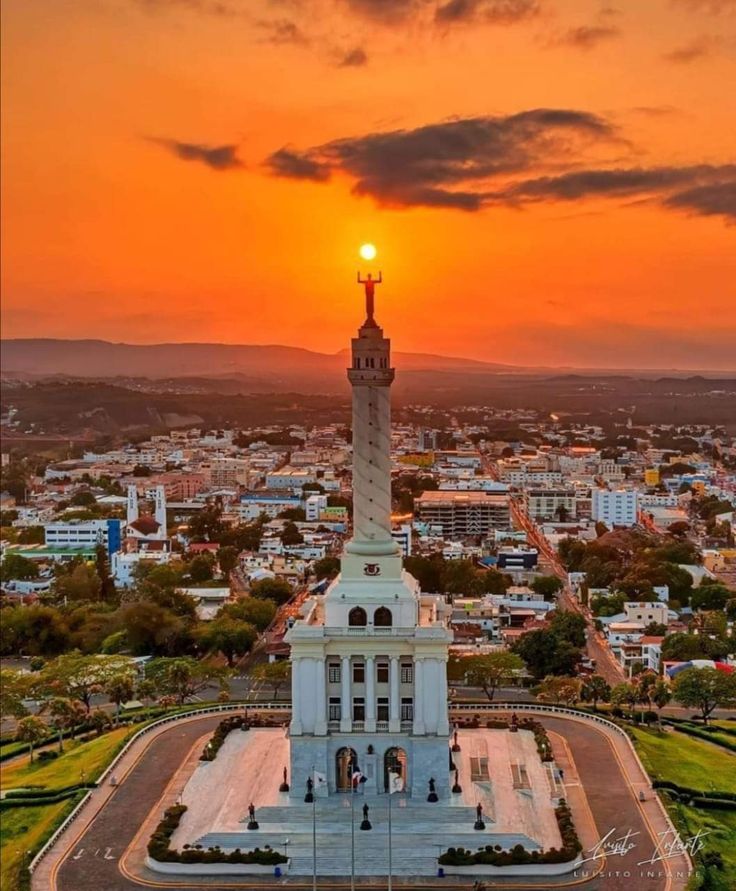 the sun is setting over a city with a monument in the foreground and buildings on the other side