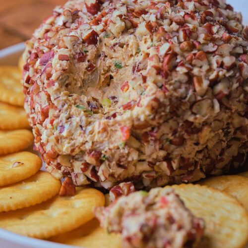 a cracker and cheese ball on top of crackers in a white bowl with red sprinkles