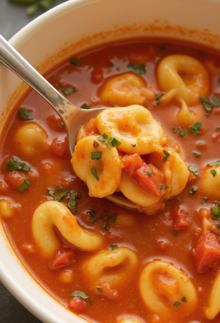 a spoon full of soup with tortellini shells in it and garnished with parsley