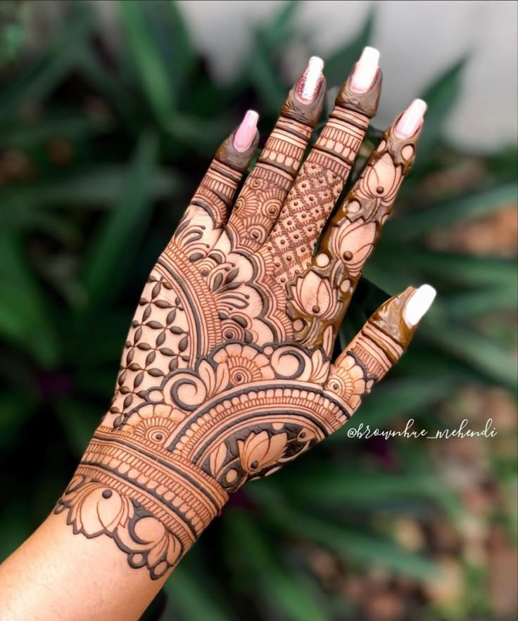 a woman's hand with henna tattoos on it and some plants in the background