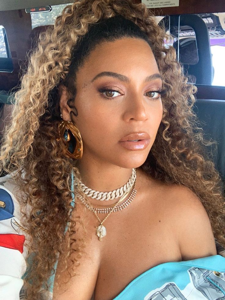 a close up of a person in a car with long curly hair and large hoop earrings