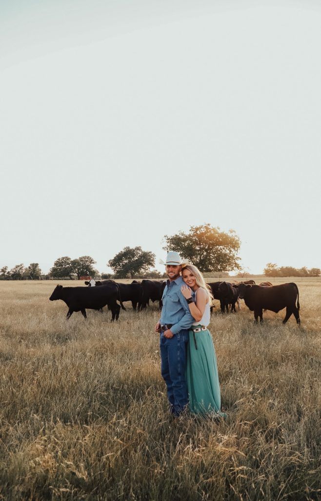 a man and woman standing in the middle of a field with cows