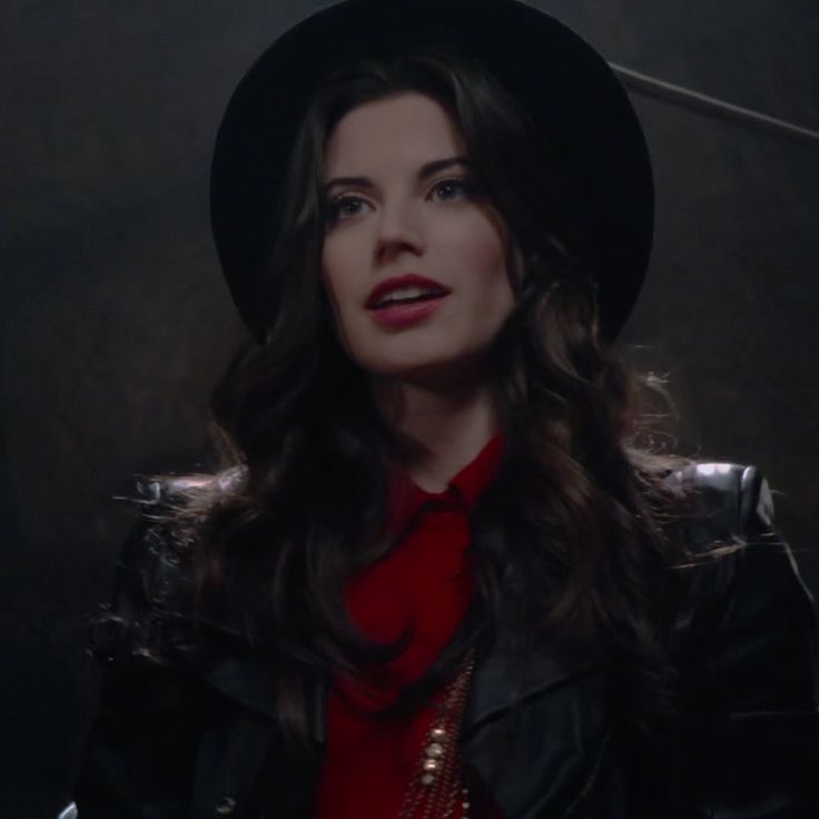 a woman wearing a black hat and red shirt in a dark room with lights on