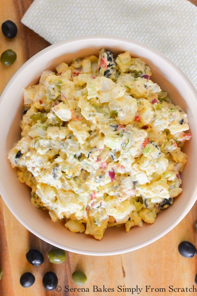 a white bowl filled with pasta salad on top of a wooden table next to olives