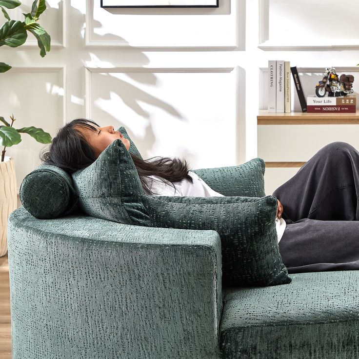 a woman laying on top of a green couch next to a potted plant in a living room