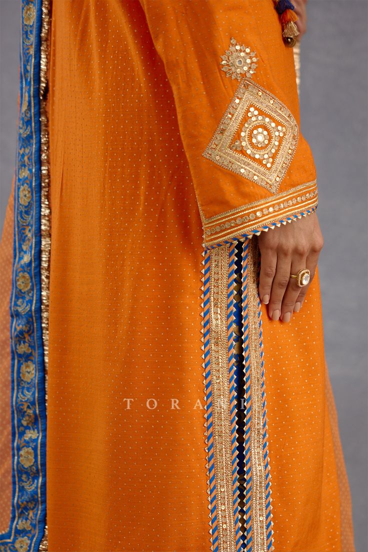 Bright orange phiran kurta with mirror and hand adda work on the yoke. Comes with chintz print salwar and sheer orange dupatta.
Components: 3
Pattern: Embroidery and Print
Type Of Work: Hand Adda Work, Mirror and Chintz Print
Neckline: Notch
Sleeve Type: Full
Fabric: Slub Silk, Cotton Silk and Silk Organza
Color: Orange
Other Details: 
Dupatta with blue printed border
Kurta with slits on the sides
Tassel detail on the yoke
Occasion: Wedding - Aza Fashions Chintz Print, Orange Dupatta, Pakistan Dress, Orange Suit, Kurta Set For Women, Pakistani Fashion Party Wear, Indian Dresses Traditional, Floral Chiffon Dress, Embroidery Suits Design