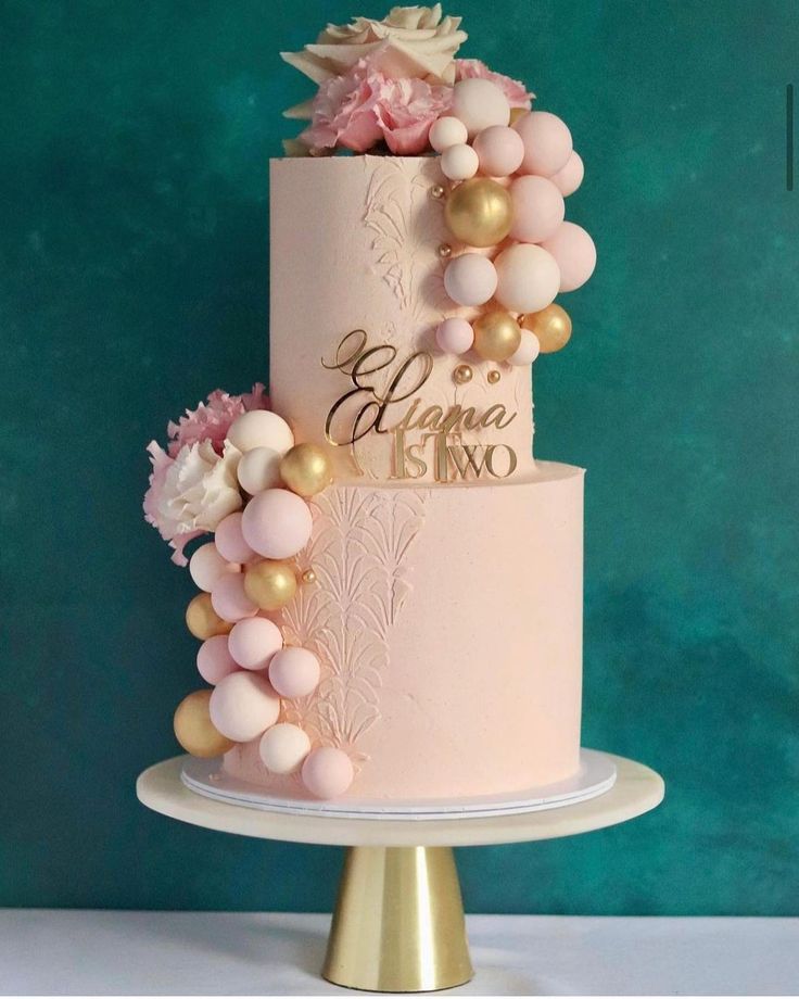 a pink and gold wedding cake with flowers on top