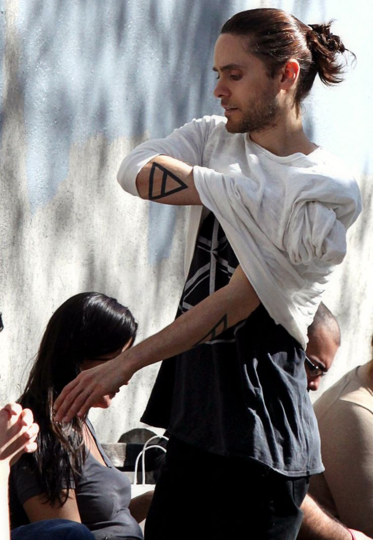 a man standing next to a woman in front of a wall with tattoos on his arms