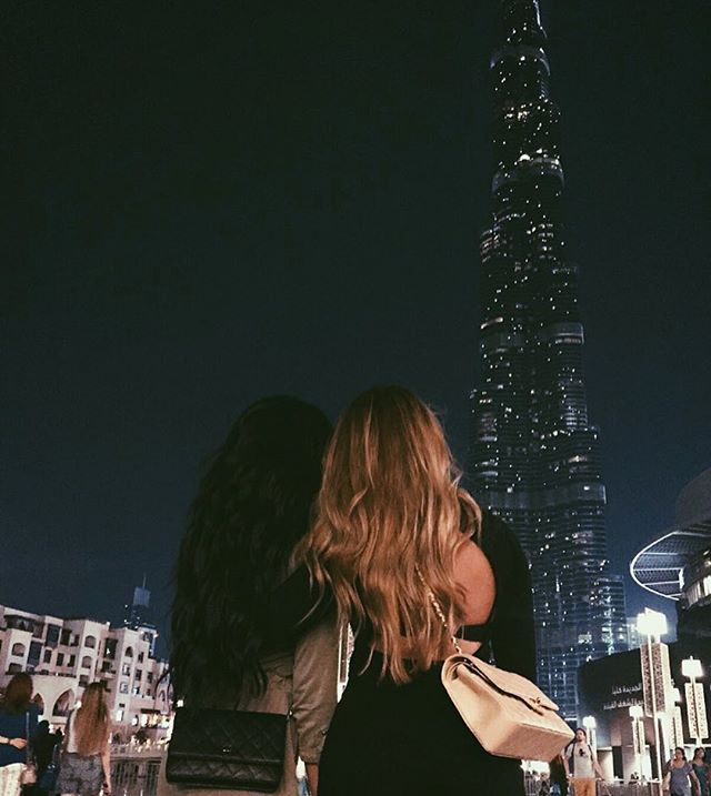 two women standing in front of a tall building at night with their backs to each other