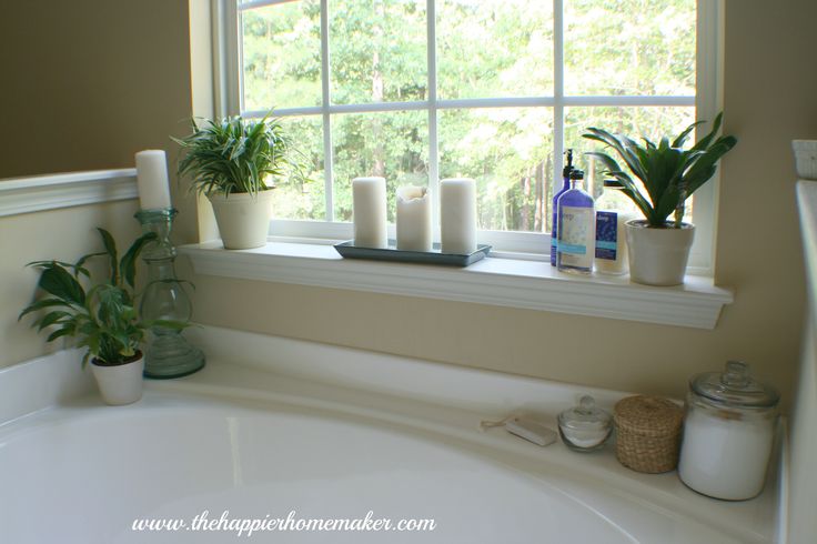 a bath tub sitting under a window next to a potted plant and two candles