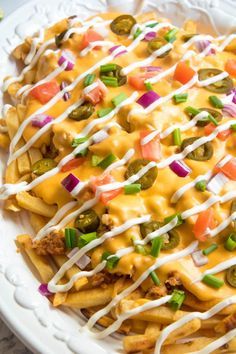 a white plate topped with cheesy fries covered in cheese and veggies