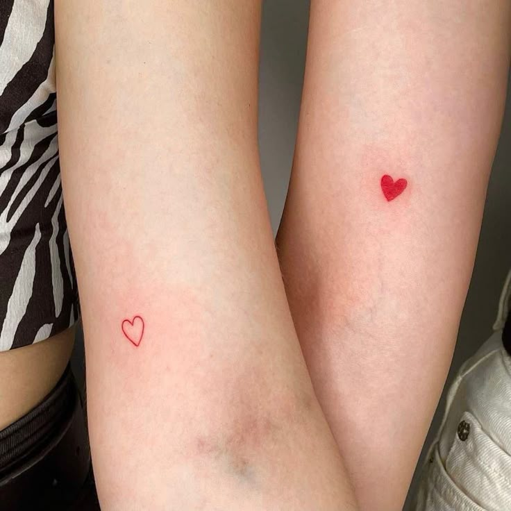 two women with small tattoos on their legs, one has a red heart in it