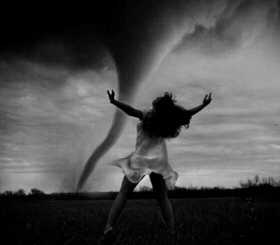 a woman is jumping in the air with her arms wide open as she stands under a storm cloud