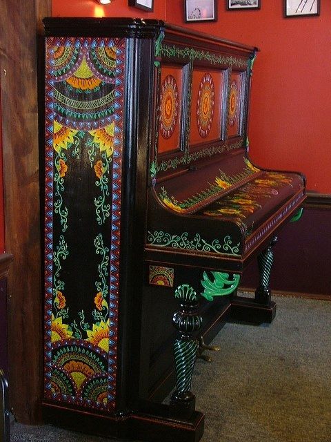 an ornately decorated upright piano in a room with red walls and pictures on the wall