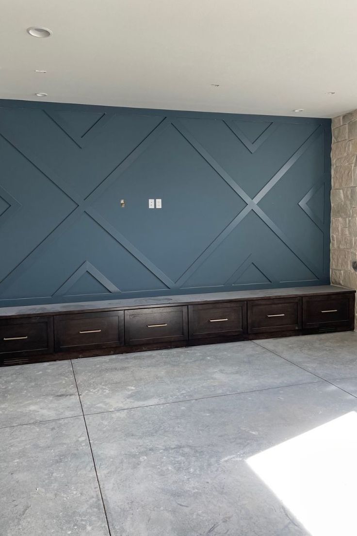 an empty room with blue walls and wooden drawers in the center, on concrete flooring