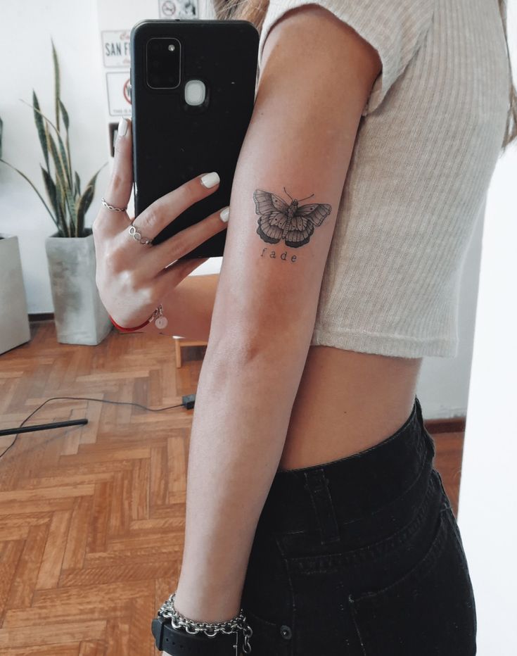 a woman with a butterfly tattoo on her arm holding a cell phone and looking at it