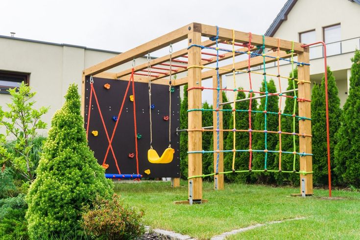 an outdoor play structure made out of wooden sticks and plasticine tubes in front of a house