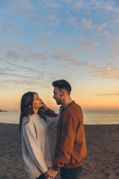 a man and woman standing on top of a beach next to the ocean at sunset