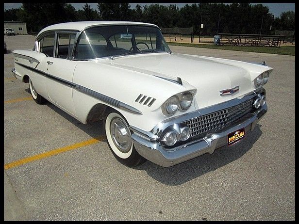 an old white car parked in a parking lot