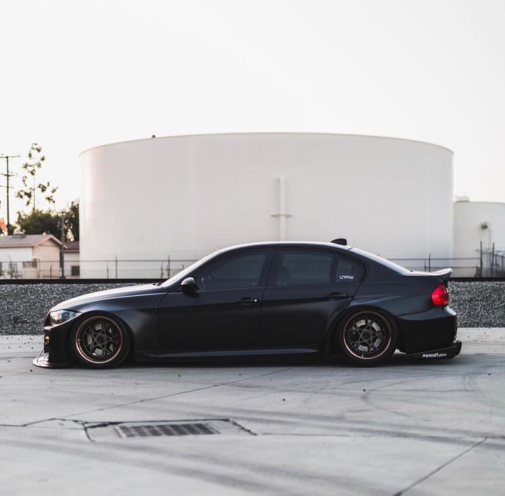 a black car parked in front of a large tank on top of a parking lot