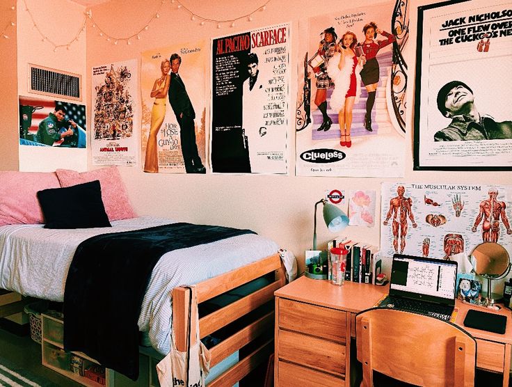 a bedroom with posters on the wall and a bed in front of it, along with two desks