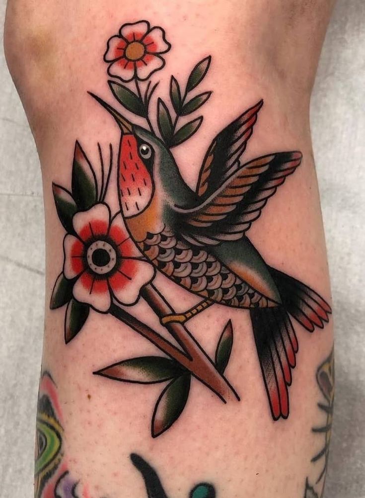 a hummingbird with flowers on its leg is shown in this tattoo design by person