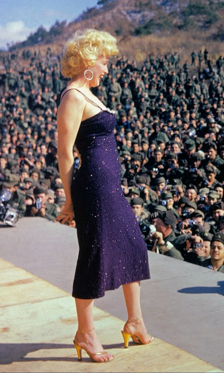 a woman in a purple dress is standing on a stage with an audience behind her