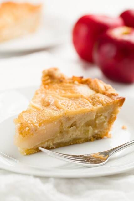 a piece of pie on a plate with a fork next to an apple in the background