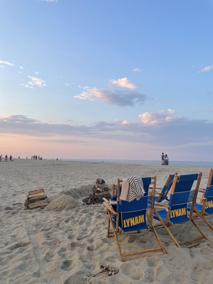 two blue lawn chairs sitting on top of a sandy beach