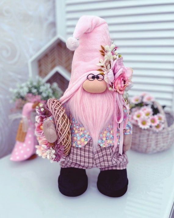 there is a small pink gnome with flowers on it's head and some baskets in the background