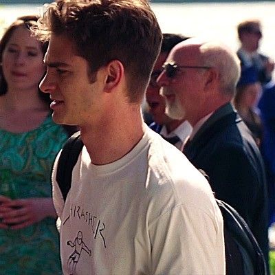 a group of people standing next to each other in front of water and grass, with one man wearing a white t - shirt