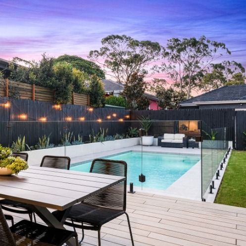 an outdoor dining table and chairs near a pool with lights on the fence around it